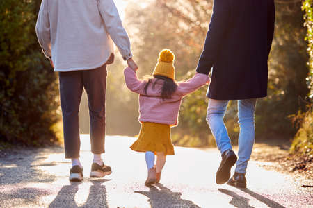 Rear View Of Family With Two Dads Taking Daughter For Walk In Fall Or Winter Countrysideの写真素材