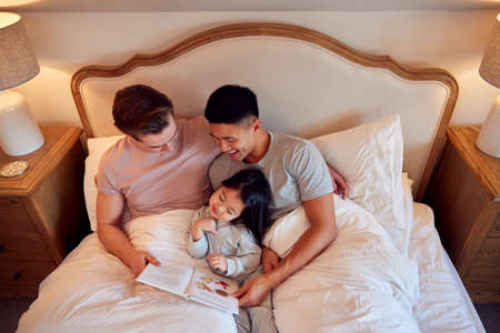 Overhead Shot Of Family With Two Dads In Bed At Home Reading Story To Daughterの写真素材