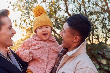 Family With Two Dads Taking Daughter For Walk In Fall Or Winter Countrysideの写真素材