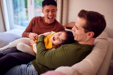Family With Two Dads On Sofa At Home Playing Game With Daughterの写真素材