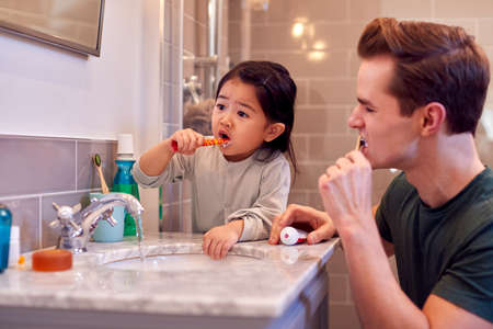 Family With Dad And Daughter Brushing Teeth In Bathroom At Home Togetherの写真素材