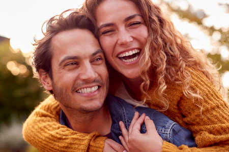 Portrait Of Happy Loving Couple With Man Giving Woman Piggyback As They Hug In Autumn Park Togetherの写真素材