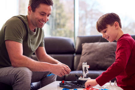 Father And Son Wearing Pyjamas Building Robotic Arm From Plastic Kit At Home