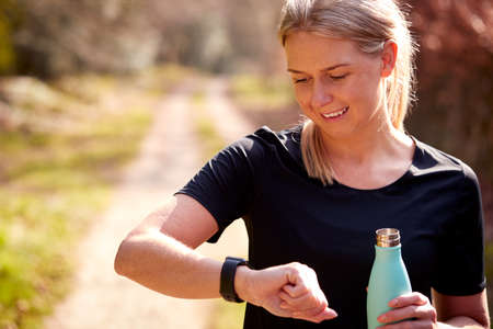 Woman With Water Bottle Checking Fitness App On Smart Watch On Run To Improve Mental Health