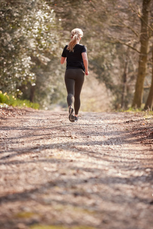 Rear View Of Young Woman Running In Autumn Countryside To Improve Mental Health During Lockdownの写真素材