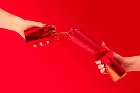 Close Up Studio Shot Of Female Hands Pulling Christmas Cracker Against Red Background