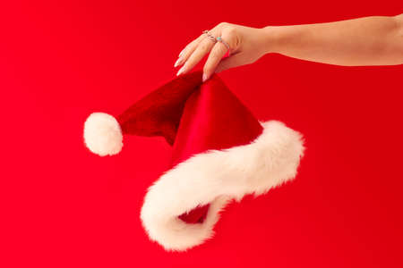 Close Up Studio Shot Of Woman Holding Christmas Santa Hat Against Red Backgroundの写真素材