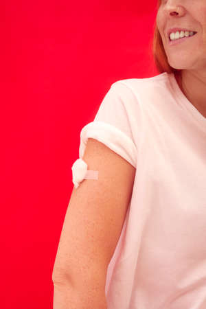 Woman With Cotton Wool Taped To Arm After Injection Or Vaccination Against Red Backgroundの写真素材