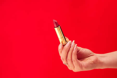 Close Up Studio Shot Of Female Hand Holding Lipstick Against Red Backgroundの写真素材