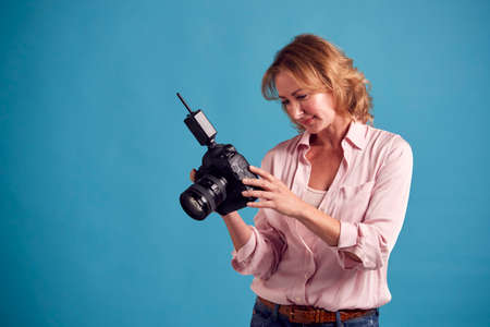 Mature Female Photographer With Camera Against Blue Background On Shoot In Studio