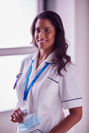 Portrait Of Female Mature Nurse In Uniform Holding Face Mask In Hospitalの写真素材