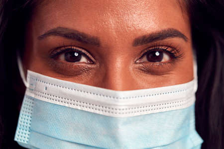 Close Up Portrait Of Female Mature Woman Wearing Face Mask In Front Of Blue Studio Backgroundの写真素材