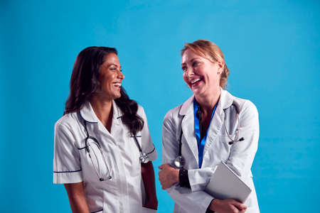 Mature Doctor And Nurse Wearing White Coat Laughing And Talking In Front Of Blue Studio Backgroundの写真素材