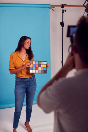 Mature Female Model Posing Against Background On Studio Shoot Holding Colour Checker Card For Videoの写真素材