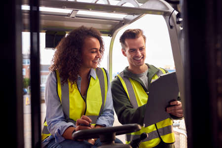 Male And Female Staff Operating Fork Lift Truck In Modern Warehouseの写真素材