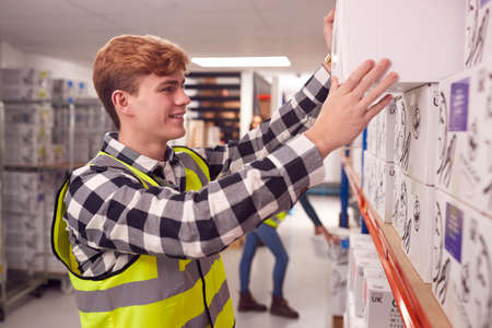 Male Worker Inside Busy Warehouse Putting Box Onto Shelf