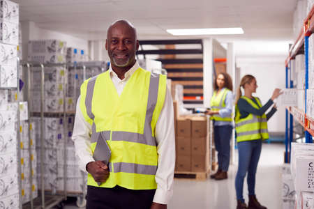 Portrait Of Team Leader With Digital Tablet In Warehouse With Staff Picking Items From Shelvesの写真素材