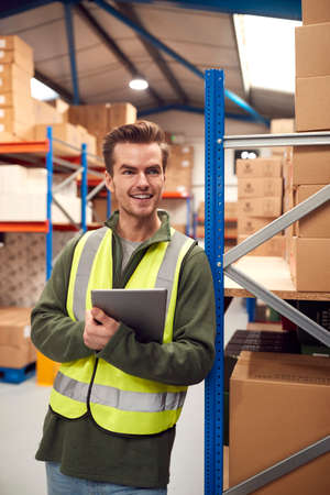 Male Worker Wearing High-Vis Vest Inside Warehouse Checking Stock On Shelves Using Digital Tabletの写真素材