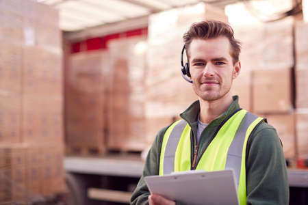 Portrait Of Male Worker At Freight Haulage Business Standing By Truck Being Loaded By Fork Liftの写真素材