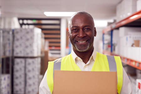 Portrait Of Smiling Male Worker Holding Box Inside Warehouseの写真素材