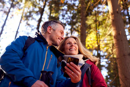 Mature Retired Couple Walk In Fall Or Winter Countryside Using Map Or Navigation App On Mobile Phone
