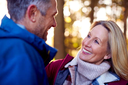 Loving Mature Retired Couple Hugging Against Autumn Countryside With Flaring Sun