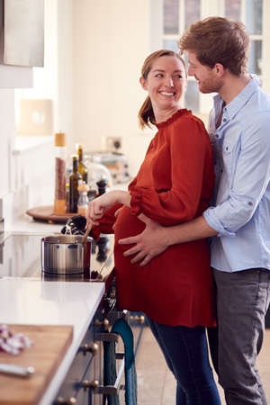 Pregnant Couple With Woman With Prosthetic Arm Preparing Meal In Kitchen Togetherの写真素材