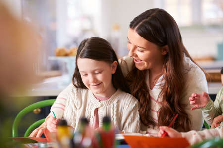 Mother And Daughter Sitting Around Table At Home Doing Craft Together