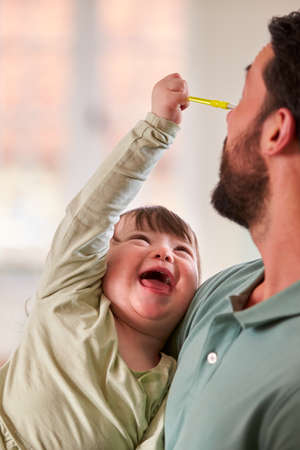 Father With Down Syndrome Daughter Sitting Around Table At Home Doing Craft Togetherの写真素材