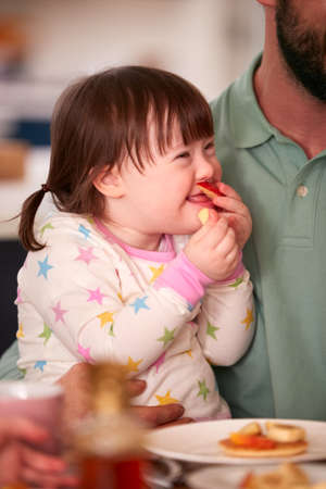 Father With Down Syndrome Daughter Sitting Around Table At Home Eating Breakfast