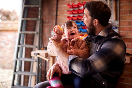 Father Sitting With Down Syndrome Daughter Eating Cupcake In Garage Workshop At Home Togetherの写真素材