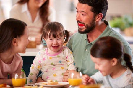 Father Making Funny Face As Family With Down Syndrome Daughter Eat Breakfast At Home