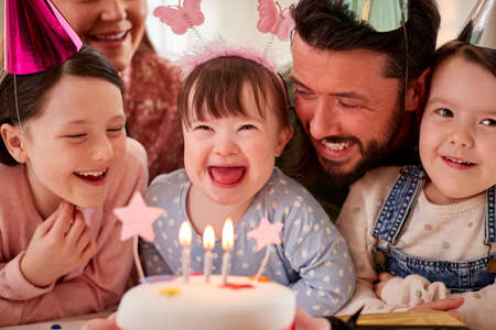 Family With Down Syndrome Daughter Celebrating Birthday With Party At Home Togetherの写真素材