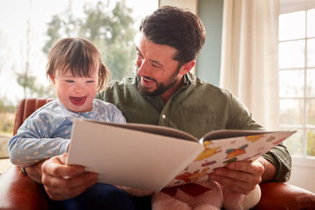 Father With Down Syndrome Daughter Reading Book At Home Togetherの写真素材