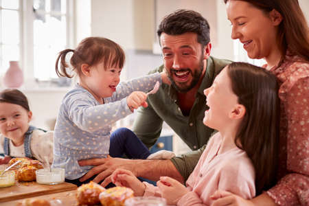Family With Down Syndrome Daughter Baking And Decorating Cakes Sitting Around Table At Homeの写真素材
