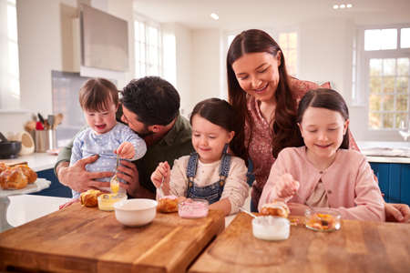Family With Down Syndrome Daughter Baking And Decorating Cakes Sitting Around Table At Homeの写真素材