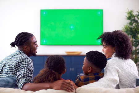 Rear View Of Family Sitting On Sofa Watching Movie On Green Screen TV At Homeの写真素材