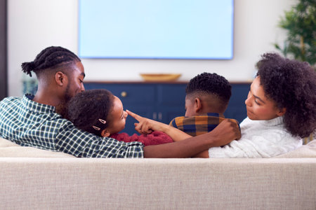 Rear View Of Family Sitting On Sofa Watching Movie On TV At Home
