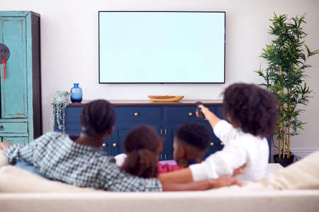 Rear View Of Family Sitting On Sofa Watching Movie On TV At Homeの写真素材