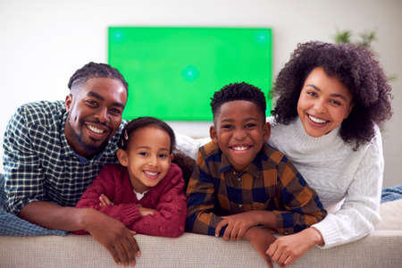 Portrait Of Family Sitting On Sofa Watching Movie On Green Screen TV At Homeの写真素材
