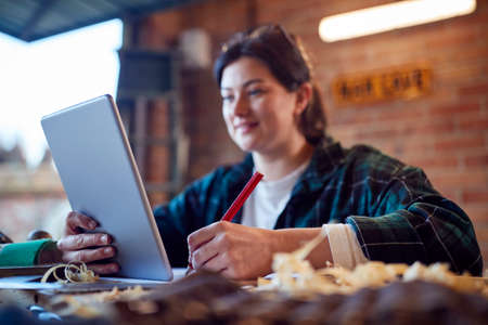 Female Carpenter In Garage Workshop Looking At Design On Digital Tabletの写真素材