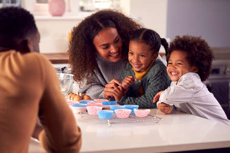 Family Baking Cupcakes Sitting Around Kitchen Counter At Home