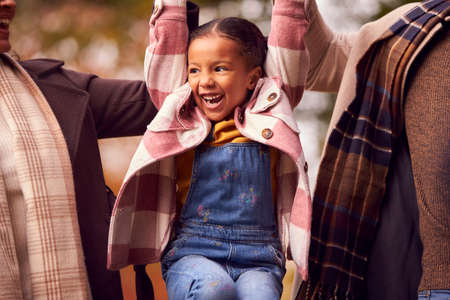 Mother And Father Lifting Daughter By Arms On Walk Through Autumn Countrysideの写真素材