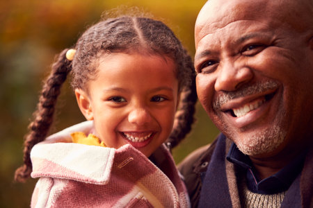 Portrait Of Grandfather Carrying Granddaughter On Walk Through Autumn Countryside Together
