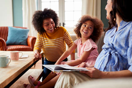 Family With Two Mums Wearing Pyjamas Reading Story Book At Home With Daughterの写真素材