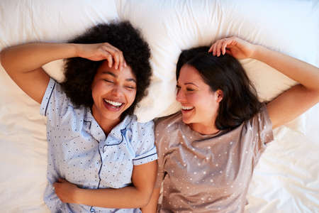 Overhead Portrait Of Loving Same Sex Female Couple Wearing Pyjamas Lying On Bed At Home