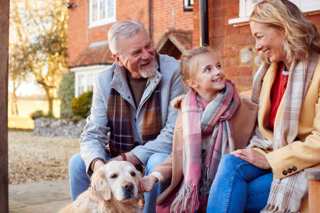 Grandparents With Granddaughter And Pet Dog Outside House Getting Ready To Go For Winter Walkの写真素材