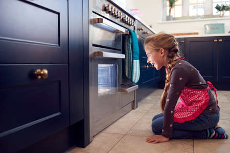 Girl Waiting By Oven In Kitchen At Home For Cakes To Bakeの写真素材