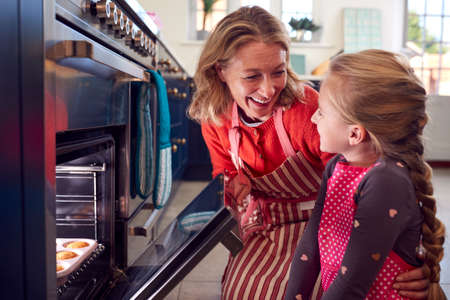 Grandmother And Granddaughter Take Freshly Baked Cupcakes Out Of The Oven In Kitchen At Homeの写真素材