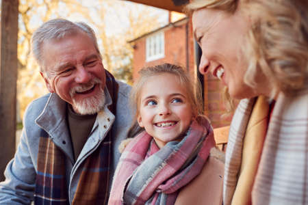 Grandparents With Granddaughter Outside House Getting Ready To Go For Winter Walkの写真素材